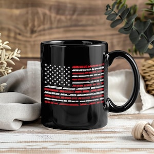 May include: Black ceramic mug with a design of the American flag. The flag's stripes are made up of red and white train illustrations, with white stars on a black background. The mug has a large handle.