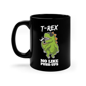 Op de afbeelding: Zwarte koffiemok met een groene cartoon T-Rex die een zonnebril draagt en de tekst "T-Rex No Like Push-Ups" erop gedrukt.