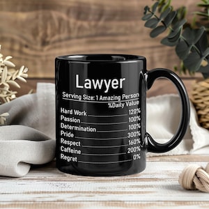 Può includere: Una tazza in ceramica nera con testo bianco che recita Lawyer, Serving Size: 1 Amazing Person, e un elenco in stile etichetta nutrizionale che include Hard Work 120%, Passion 100%, Determination 100%, Pride 300%, Respect 160%, Caffeine 200%, Regret 0%.