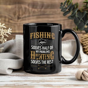 Op de afbeelding: Zwarte keramische mok met een gebogen handvat. De mok heeft de tekst "FISHING SOLVES HALF OF MY PROBLEMS HUNTING SOLVES THE REST" in goud, samen met een visafbeelding en gekruiste pijlen.