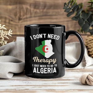 以下が含まれることがあります： 「I DON'T NEED Therapy I JUST NEED TO GO TO ALGERIA」の文字が入った黒いセラミックマグカップ。アルジェリアの国旗と地図の輪郭が描かれています。ハンドルは黒色です。