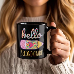 Peut inclure: Mug en céramique noire avec les mots "hello SECOND GRADE" dans des lettres colorées et fantaisistes. Un grand dessin de crayon coloré est présenté sous le mot "hello". Le mug est tenu par une personne.