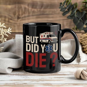 May include: A black ceramic mug featuring a graphic of an ambulance and a blue Star of Life medical symbol. The text printed on the front reads BUT DID YOU DIE? in large, bold, stacked lettering with white and red colors against the black background.