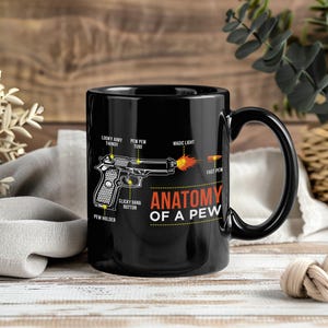 Peut inclure: Mug en céramique noire avec une anse noire. Il présente un schéma d'arme à feu avec le texte "ANATOMY OF A PEW". Le schéma comprend des étiquettes telles que "LOOKY AIMY THINGY", "PEW PEW TUBE" et "CLICKY BANG BUTTON".