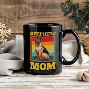 May include: Black ceramic mug with a German Shepherd design and the text "SHEPHERD MOM" in yellow. The dog illustration is set against a retro-style striped background in various colors.