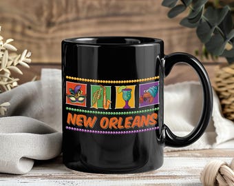 May include: Black ceramic mug with a handle featuring a colorful New Orleans design. The design includes a mask, saxophone, cocktail, and a crawfish. The words "NEW ORLEANS" are printed in orange and white.