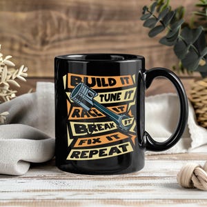 May include: Black ceramic mug with a handle, featuring the text "BUILD IT TUNE IT RACE IT BREAK IT FIX IT REPEAT" in white, yellow, and orange. A piston graphic is in the center of the text.