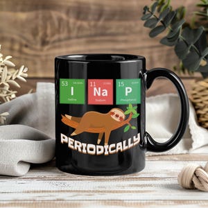 May include: Black ceramic mug featuring a sloth graphic and the word "Periodically." The design incorporates elements from the periodic table, including the symbols for iodine, sodium, and phosphorus. The mug has a black handle.