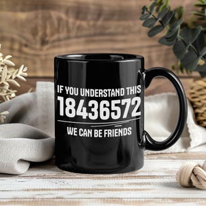 以下が含まれることがあります： 「IF YOU UNDERSTAND THIS 18436572 WE CAN BE FRIENDS」の白い文字が入った黒いセラミックコーヒーマグ。マグカップには大きなハンドルがあり、木製の背景に置かれています。