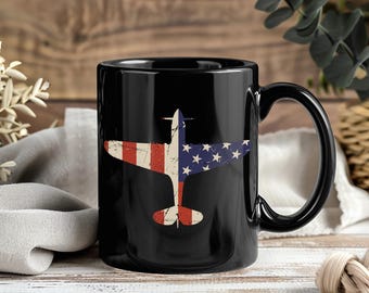 May include: Black ceramic mug featuring a distressed graphic of an airplane with the American flag design. The mug has a large handle and a glossy finish. The airplane design incorporates red and white stripes and blue stars.