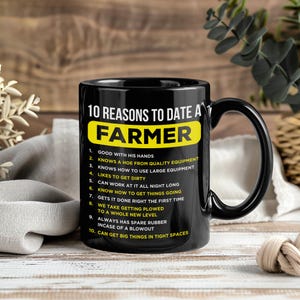 May include: Black ceramic mug with a large handle. The mug features the text "10 REASONS TO DATE A FARMER" in white and yellow, with a list of reasons below. The mug is on a wooden surface.
