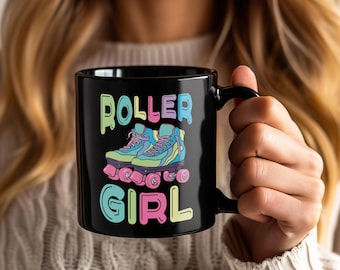 May include: Black ceramic mug featuring the words "ROLLER GIRL" in colorful bubble letters. The mug displays a graphic of roller skates in shades of blue, pink, and yellow, evoking a retro aesthetic.