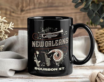 May include: Black ceramic mug featuring a New Orleans design. The mug has a trumpet, saxophone, and musical notes graphic. The text "NEW ORLEANS" and "BOURBON ST." are also displayed on the mug.