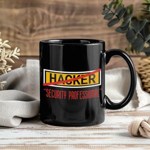 Puede incluir: Taza de cerámica negra con asa curva. La taza presenta la palabra "HACKER" tachada en rojo, con "SECURITY PROFESSIONAL" en rojo debajo. La taza está sobre un fondo de madera.