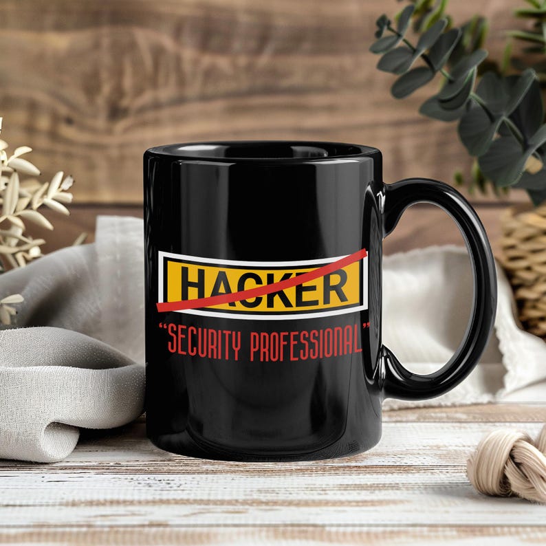 K&ouml;nnte beinhalten: Schwarze Keramik-Tasse mit gebogenem Henkel. Die Tasse zeigt das Wort "HACKER" rot durchgestrichen, darunter "SECURITY PROFESSIONAL" in Rot. Die Tasse steht vor einem Holzgrund.