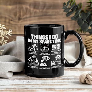 May include: A black ceramic mug featuring white text that reads "THINGS I DO IN MY SPARE TIME" followed by six illustrations depicting cross-country skiing activities, including watching, researching, talking, thinking, and dreaming about skiing.
