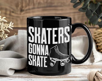 May include: Black ceramic mug with the text "SKATERS GONNA SKATE" in white, along with a white roller skate graphic. The mug has a black handle and is set against a wooden background.