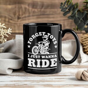 以下が含まれることがあります： 白いモトクロスライダーのグラフィックと「FORGET TOYS I JUST WANNA RIDE」のテキストが特徴の黒いセラミックマグ。マグカップは黒いハンドルと光沢のある仕上げが施されています。デザインはマグカップの中央に配置されています。