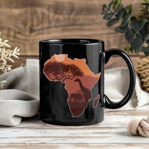 May include: Black ceramic mug featuring a silhouette of the African continent in shades of brown and orange. The design includes a tree, giraffe, and elephants, with a sun in the background. The mug has a curved handle.