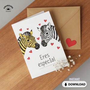 May include: A greeting card with two zebra heads, one yellow and black, the other black and white, surrounded by red hearts. The card reads "Eres especial" and is accompanied by a brown envelope and a sprig of white flowers.