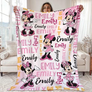 A woman is holding up a large blanket with Minnie Mouse and Emily characters printed on it.