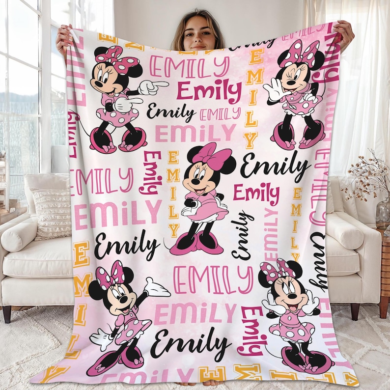 A woman is holding up a large blanket with Minnie Mouse and Emily characters printed on it.