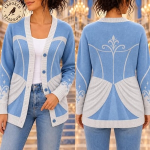 May include: A light blue and silver knit cardigan featuring a button-front closure and a white trim along the collar and cuffs. The garment displays a decorative silver pattern on the front and back, with small star accents on the sleeves.