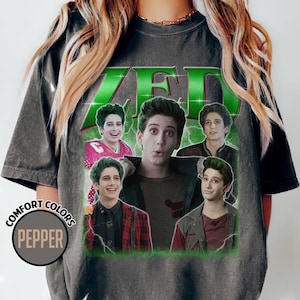 May include: Dark gray t-shirt featuring a graphic of a young man with green hair and the word "ZED" in green. The graphic includes multiple images of the same person. The shirt has the words "COMFORT COLORS" and "PEPPER" in a circle.