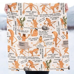 May include: A cream-colored blanket featuring a repeating pattern of cartoonish, elongated figures in various poses. The figures are in shades of brown and tan, with speech bubbles and phrases like "It's making me mad" and "I don't like this rock".