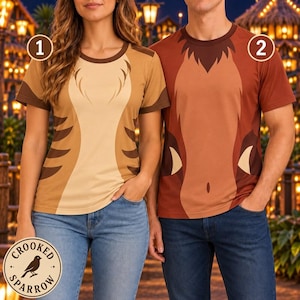 May include: Two short-sleeve t-shirts featuring animal-inspired patterns. Shirt one is light tan with dark brown side stripes and a round neck. Shirt two is a darker reddish-brown with a central lighter panel and a round neck. Both have numbered labels.