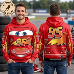 May include: A red hooded sweatshirt featuring a graphic print of a race car with the number 95, yellow lightning bolts, and checkered patterns. The front displays the car's face, while the back shows the rear of the car with the number 95.