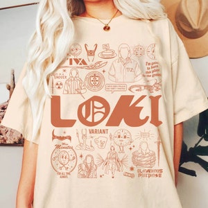 May include: Cream-colored t-shirt featuring a brown graphic design with the word "LOKI" in large letters. The design includes various illustrations and the text "VARIANT", "Miss Minutes", and "Glorious Purpose".