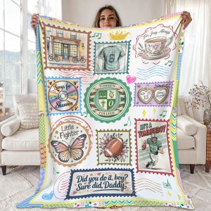 May include: A white blanket featuring various postage stamp-style designs. The stamps include a football, a butterfly, a college crest, and the text "He's a Tommenboy." Other stamps have text like "Songs for Shannon" and "Did you do it, boy? Sure did, Daddy."