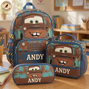 May include: A blue and brown backpack, lunch bag, and pencil case set featuring a cartoon tow truck character with green eyes and the name ANDY printed in white. The items have a rusted metal texture design with yellow and black hazard stripes.