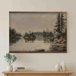 K&ouml;nnte beinhalten: Ein gerahmtes Landschaftsgem&auml;lde zeigt eine ruhige See mit Inseln und B&auml;umen. Das Kunstwerk h&auml;ngt &uuml;ber einem Konsolentisch aus hellem Holz, erg&auml;nzt durch dekorative Vasen, eine Topfpflanze und einen beigen Sessel mit einer Decke.
