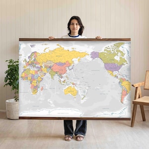 Può includere: Una grande mappa del mondo rettangolare incorniciata in legno scuro. La mappa presenta uno sfondo oceanico grigio chiaro con continenti raffigurati in vari colori pastello tra cui giallo, viola, rosa e verde, con etichette nere per i paesi.
