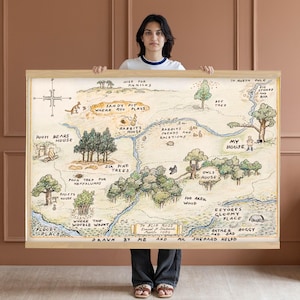 May include: A framed map illustration of a whimsical forest landscape with text labels like "Pooh Bear's House" and "100 Acre Wood." The artwork features a light brown wooden frame and a detailed, hand-drawn style.