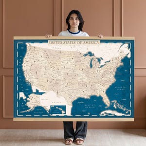 Puede incluir: Un mapa grande de los Estados Unidos de América, exhibido en un marco de madera. El mapa presenta un diseño vintage con un fondo crema y bordes azul oscuro. El texto "UNITED STATES OF AMERICA" está en la parte superior.