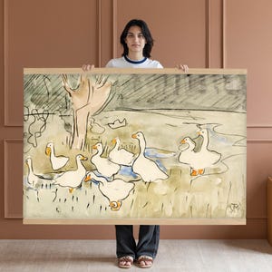May include: A framed watercolor painting featuring a flock of white geese in a field. The artwork has a light brown wooden frame. The geese have orange beaks and feet. The background includes a tree and a cloudy sky.
