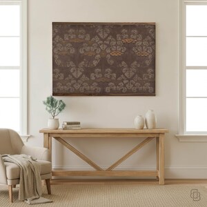 K&ouml;nnte beinhalten: Ein rechteckiges Wandkunstwerk mit dunkelbraunem Hintergrund und einem sich wiederholenden Blumenmuster in Grau- und Goldt&ouml;nen. Das Kunstwerk ist in dunklem Holz gerahmt. Der Raum umfasst eine Konsole aus hellem Holz, einen beigen Sessel und zwei wei&szlig;e Vasen.