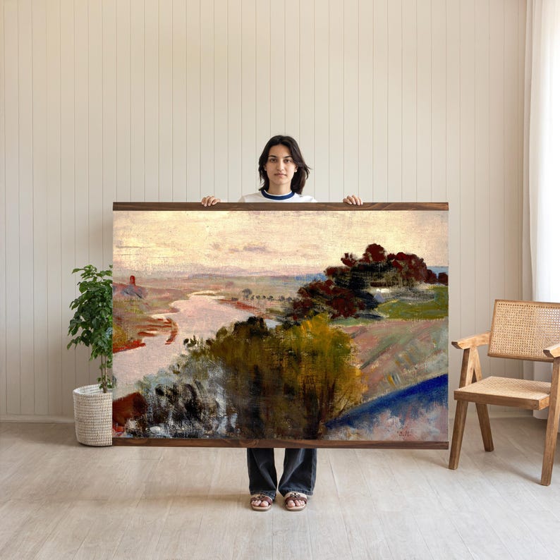 May include: A large rectangular landscape painting featuring a winding river flowing through a valley with trees in shades of green, yellow, and dark red. The sky is a pale, soft tone, and the artwork is framed in a simple, dark brown wooden border.