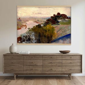 May include: A rectangular landscape painting in a light wood frame depicting a river winding through a valley with dark green and yellow trees in the foreground, rolling hills in the distance, and a pale, overcast sky above the horizon.