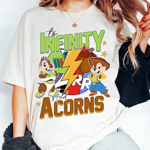 May include: White t-shirt with a graphic design featuring two cartoon chipmunks, one dressed as Buzz Lightyear and the other as Woody from Toy Story. The design also includes a lightning bolt and the text "to infinity and acorns".