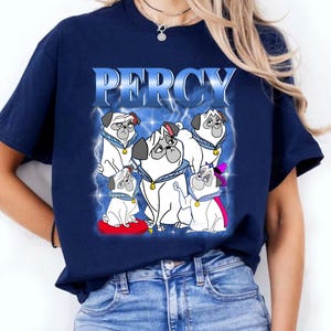 Pode incluir: Camiseta azul marinho com um desenho de v&aacute;rios c&atilde;es pug de desenho animado e o nome "PERCY". Os pugs s&atilde;o brancos com detalhes em preto e usam acess&oacute;rios. O texto "PERCY" est&aacute; em uma fonte azul com raios.