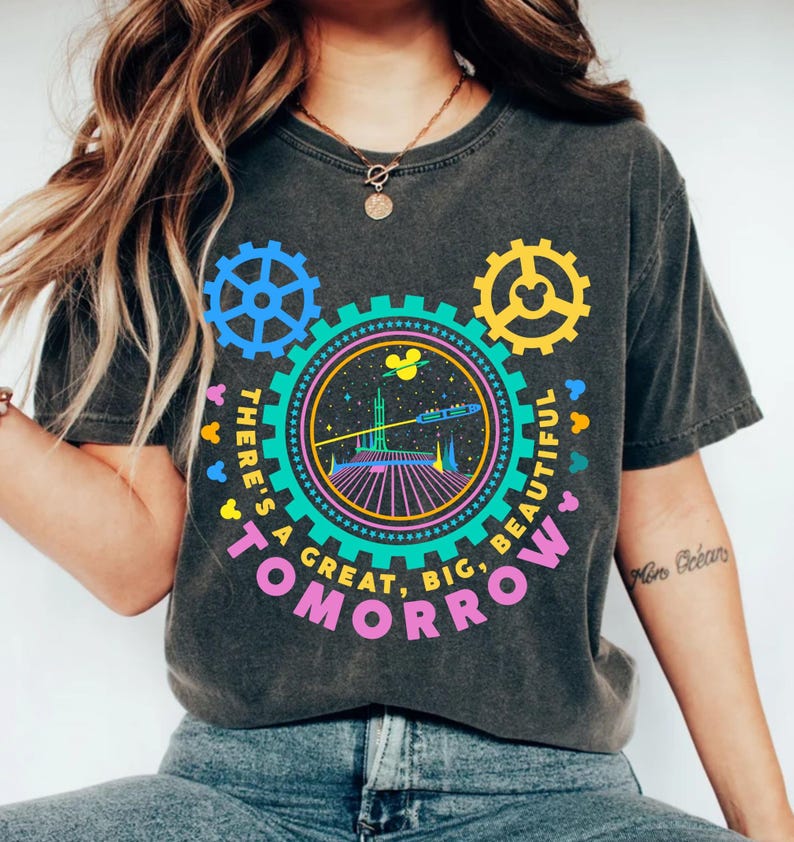 May include: A charcoal grey t-shirt featuring a colourful graphic of a futuristic space scene inside a large gear. The design includes the text "THERE'S A GREAT, BIG, BEAUTIFUL TOMORROW" in pink, with smaller gear shapes and mouse silhouettes.