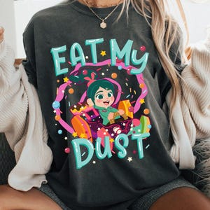 May include: A charcoal gray crewneck t-shirt featuring a colorful graphic of a cartoon character driving a candy-themed race car. The text EAT MY DUST is printed in large light blue letters above and below the central illustration of the character.