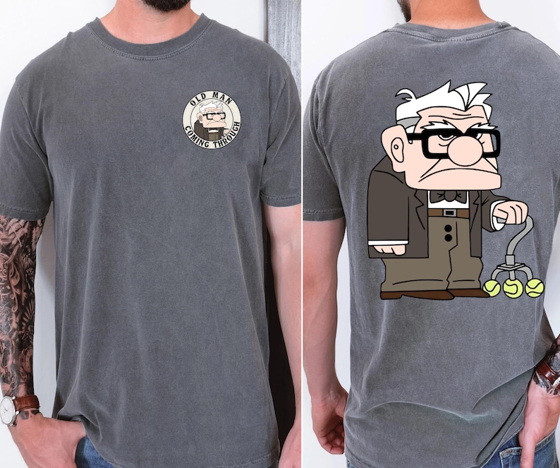 May include: Charcoal gray t-shirt featuring a cartoon illustration of an elderly man with glasses and a cane holding tennis balls. The front of the shirt has a circular graphic with the text "OLD MAN COMING THROUGH".