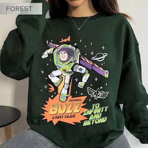 K&ouml;nnte beinhalten: Dunkelgr&uuml;nes Sweatshirt mit einem Buzz Lightyear-Motiv. Das Design zeigt Buzz in Aktion, mit den Worten "Original Buzz Lightyear" und "To Infinity and Beyond". Die Grafik ist im Cartoon-Stil gehalten, mit Weltraum-Elementen.