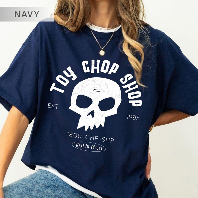Pu&ograve; includere: Una t-shirt blu navy a maniche corte con una grafica bianca raffigurante un teschio e il testo TOY CHOP SHOP, EST. 1995, 1800-CHP-SHP e Rest in Pieces. Il design presenta una texture usurata ed &egrave; centrato sulla parte anteriore del capo.