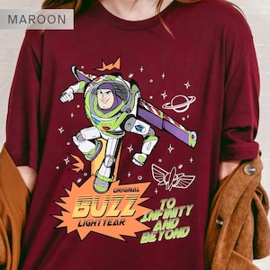 K&ouml;nnte beinhalten: Burgunderfarbenes Langarm-T-Shirt mit einer Grafik von Buzz Lightyear. Das Design enth&auml;lt den Text "ORIGINAL BUZZ LIGHTYEAR" und "TO INFINITY AND BEYOND" in einer stilisierten Schriftart, mit Weltraum-Akzenten.